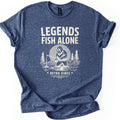 Legends Fish Alone Bigfoot Comfort Colors T-shirt in Heather Navy, laid flat. Cream print of Bigfoot fishing knee-deep in a lake before a light gray moon and pine trees, under the words Legends Fish Alone and above Retro Vibes between two stars. Sleeves cuffed, on a white background.