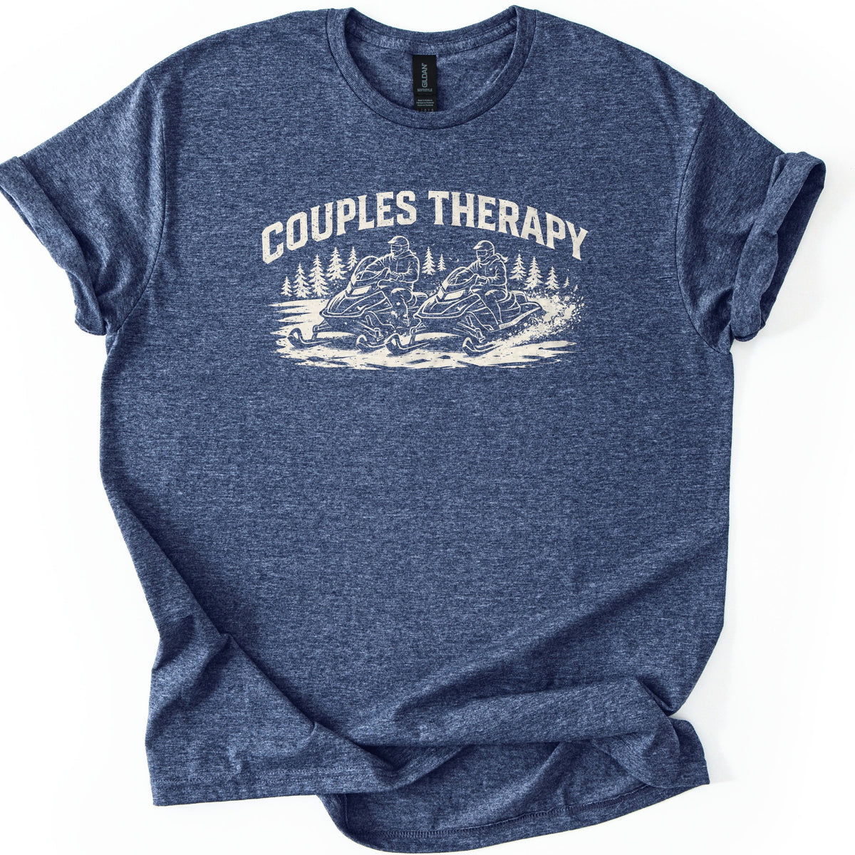 Couples Therapy Snowmobile Comfort Colors T-shirt in Heather Navy, laid flat. Cream print of the arched words Couples Therapy above two helmeted riders on snowmobiles racing side by side through snow with pine trees behind. Sleeves are cuffed on a white background.