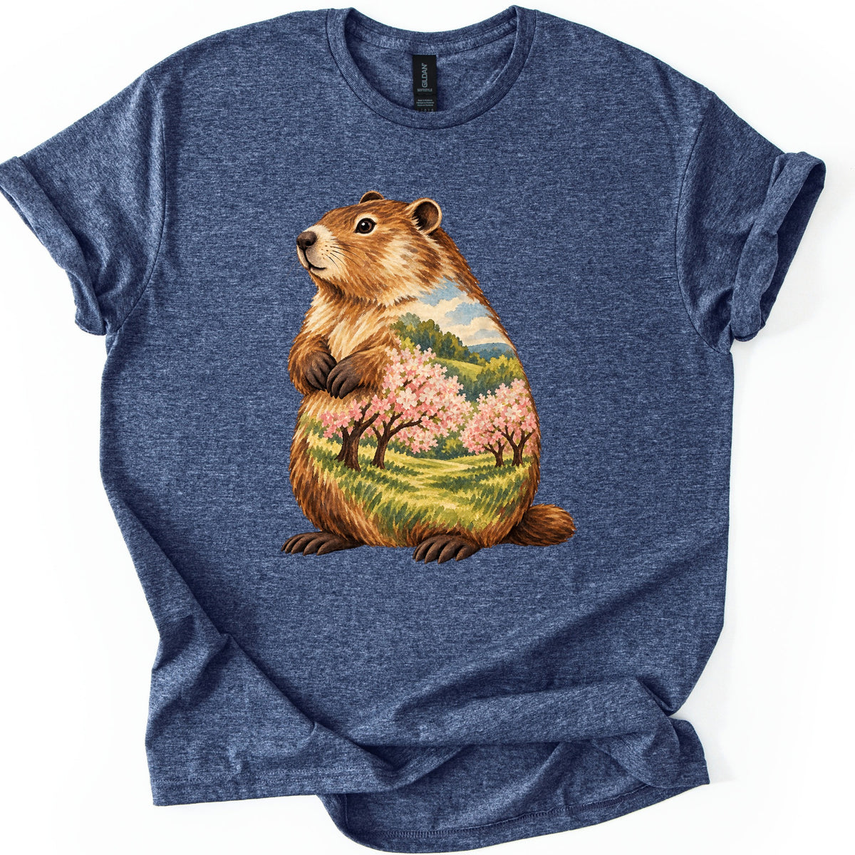 Groundhog Blossom Meadow Comfort Colors T-shirt in Heather Navy, laid flat. A painted groundhog sits upright with paws at its chest, its body filled with a meadow of pink blossoming trees, green hills and blue sky. No words. Sleeves cuffed, on a white background.