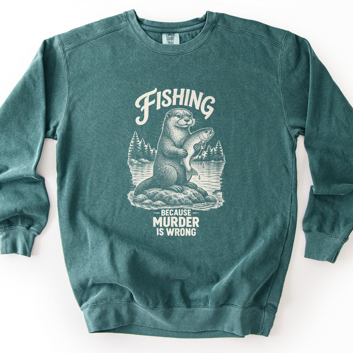 Fishing Because Murder Is Wrong Comfort Colors crewneck sweatshirt in Blue Spruce, laid flat. A cream sketch of an otter sitting on a lake rock holds a dripping trout, with pine trees behind it. Fishing arches overhead and Because Murder Is Wrong is printed below. Laid on a white surface.