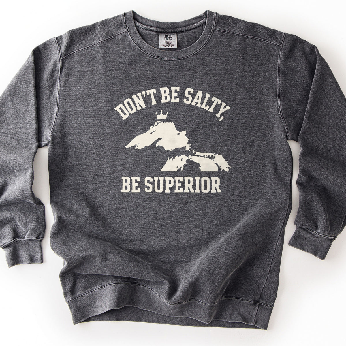 Be Superior Comfort Colors crewneck sweatshirt in Pepper, laid flat. Cream print of the words Don't Be Salty, arched above a silhouette of Lake Superior topped with a small crown, with Be Superior below. Laid on a white background.
