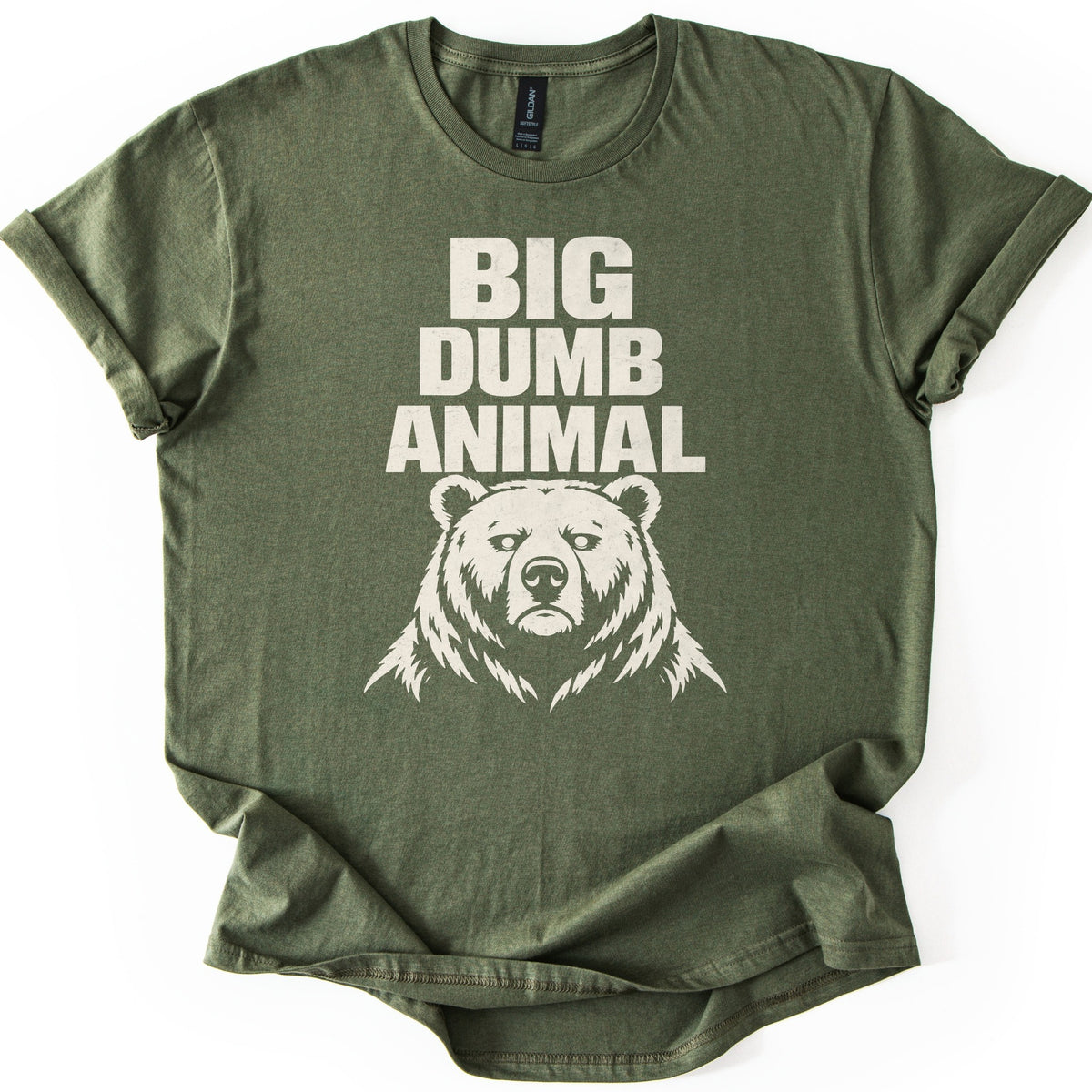 Big Dumb Animal Comfort Colors T-shirt in Military Green, laid flat. Bold cream letters read BIG DUMB ANIMAL above a cream illustration of a stern, front-facing bear head with shaggy fur. The sleeves are rolled and the shirt lies on a white background.