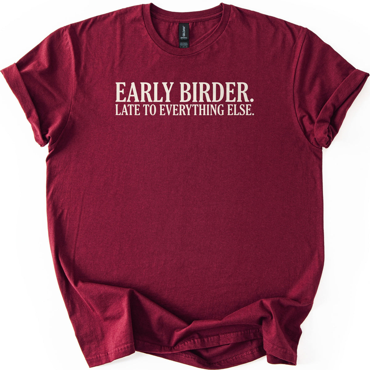 Early Birder Comfort Colors T-shirt in Maroon, laid flat. Cream serif capital letters across the chest read EARLY BIRDER. LATE TO EVERYTHING ELSE. The shirt lies on a white background with its short sleeves rolled up.