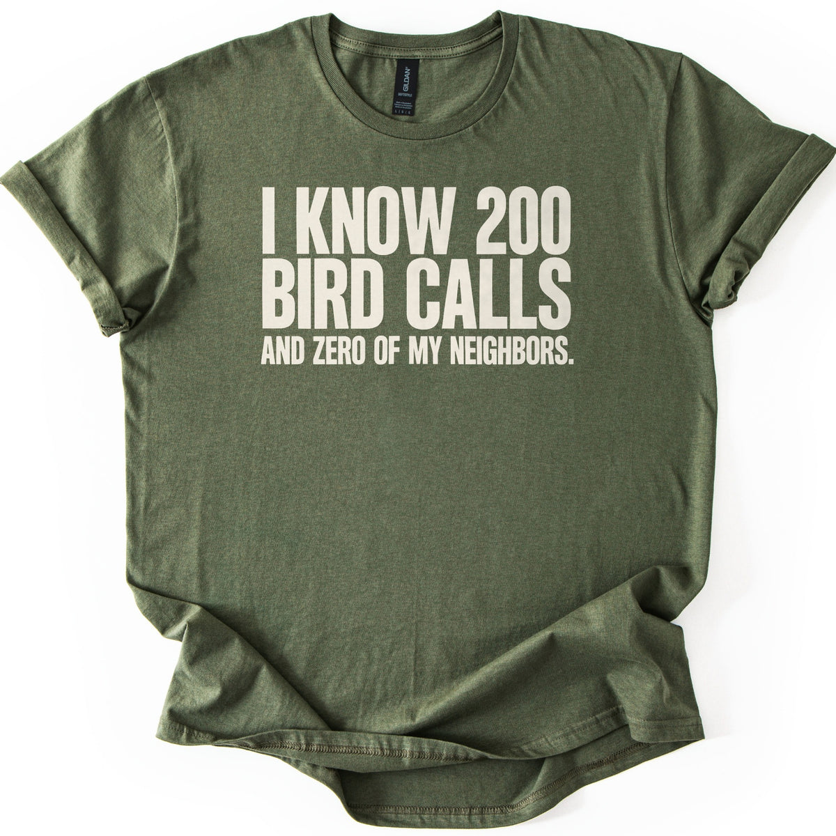 I Know 200 Bird Calls and Zero of My Neighbors Comfort Colors T-shirt in Military Green, laid flat. Bold cream capital letters across the chest read I Know 200 Bird Calls and Zero of My Neighbors. The heathered shirt lies on a white background with rolled sleeves and a rumpled hem.