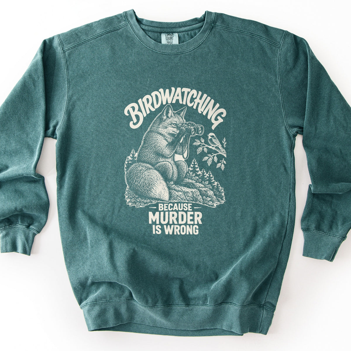 Birdwatching Because Murder Is Wrong Comfort Colors crewneck sweatshirt in Blue Spruce, laid flat. A cream sketch of a fox on a rock using binoculars to watch a small bird on a leafy branch, with pine trees behind. Birdwatching arches above; Because Murder Is Wrong is below. White background.