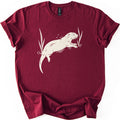 Swimming Otter Comfort Colors T-shirt in Maroon, laid flat. A cream linocut-style otter swims through rippling water between tall reeds, with droplets above its head. No words are printed. The sleeves are cuffed and the shirt lies on a white background.