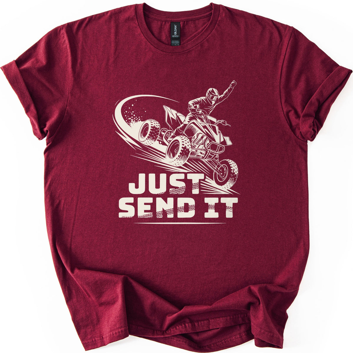 ATV Just Send It Comfort Colors T-shirt in Maroon, laid flat. A cream illustration shows a helmeted rider on a quad ATV mid-air, fist raised, with a swoosh of dust, above the words Just Send It in bold tire-marked letters. Sleeves are cuffed, on a white background.