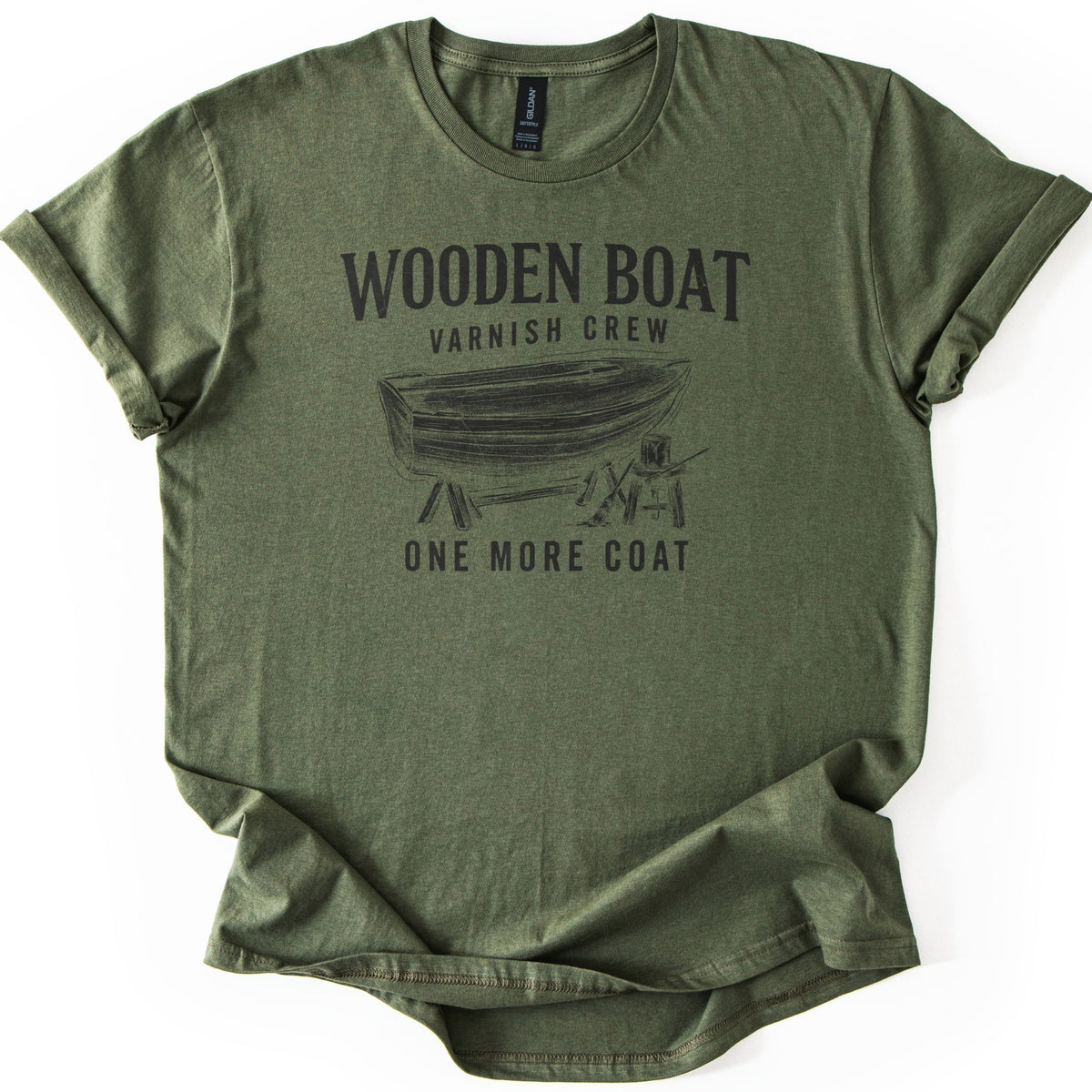 Wooden Boat Varnish Crew Comfort Colors T-shirt in Military Green, laid flat. Black print reads Wooden Boat, Varnish Crew above a sketch of a wooden rowboat on sawhorses beside a stool with a varnish can and brush, then One More Coat. Sleeves cuffed on a white background.