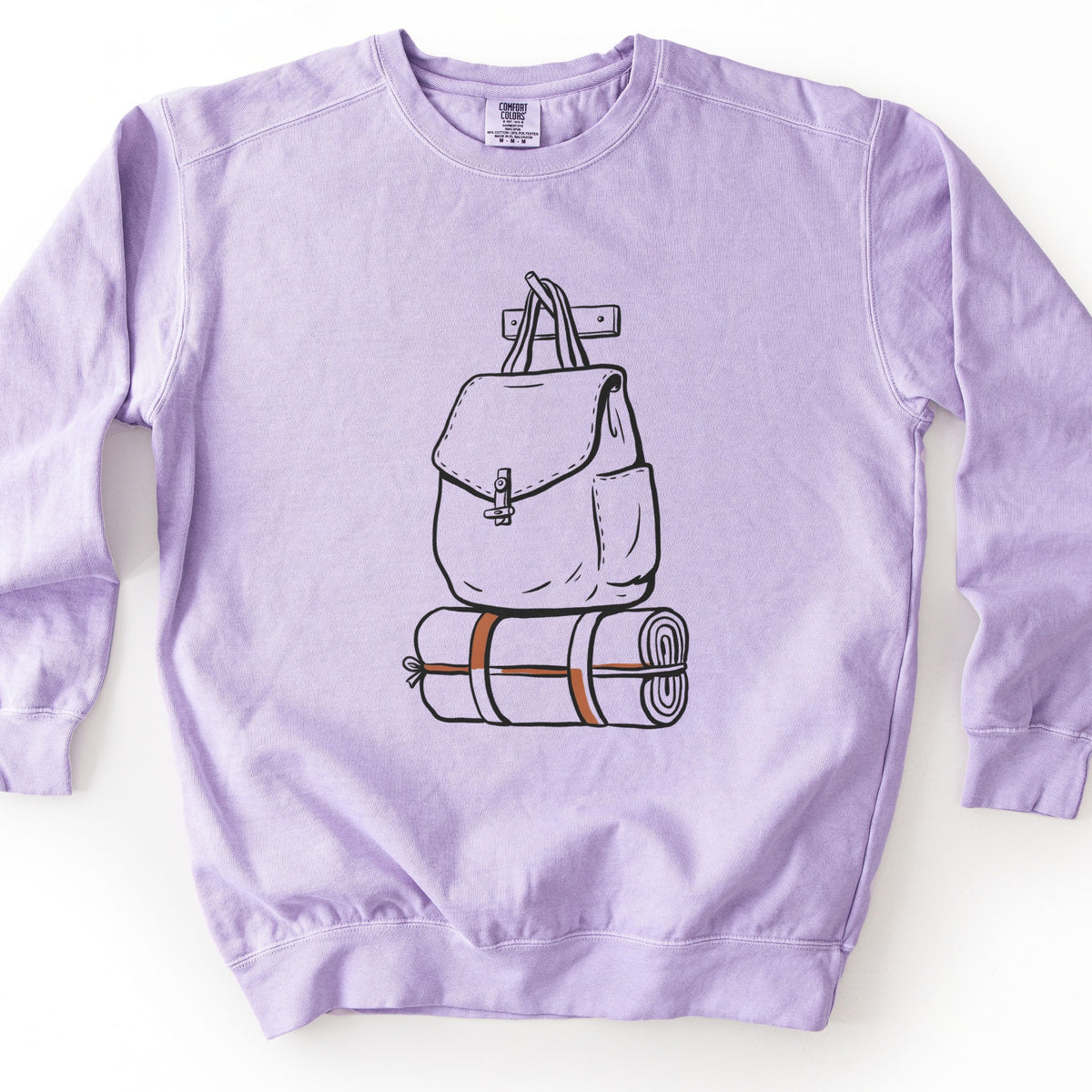 Backpack And Bedroll Comfort Colors crewneck sweatshirt in Orchid, laid flat. Black line art of a canvas backpack with a toggle clasp hanging by its straps from a wall peg above a rolled bedroll tied with orange straps. No words are printed. Shown on a white background.