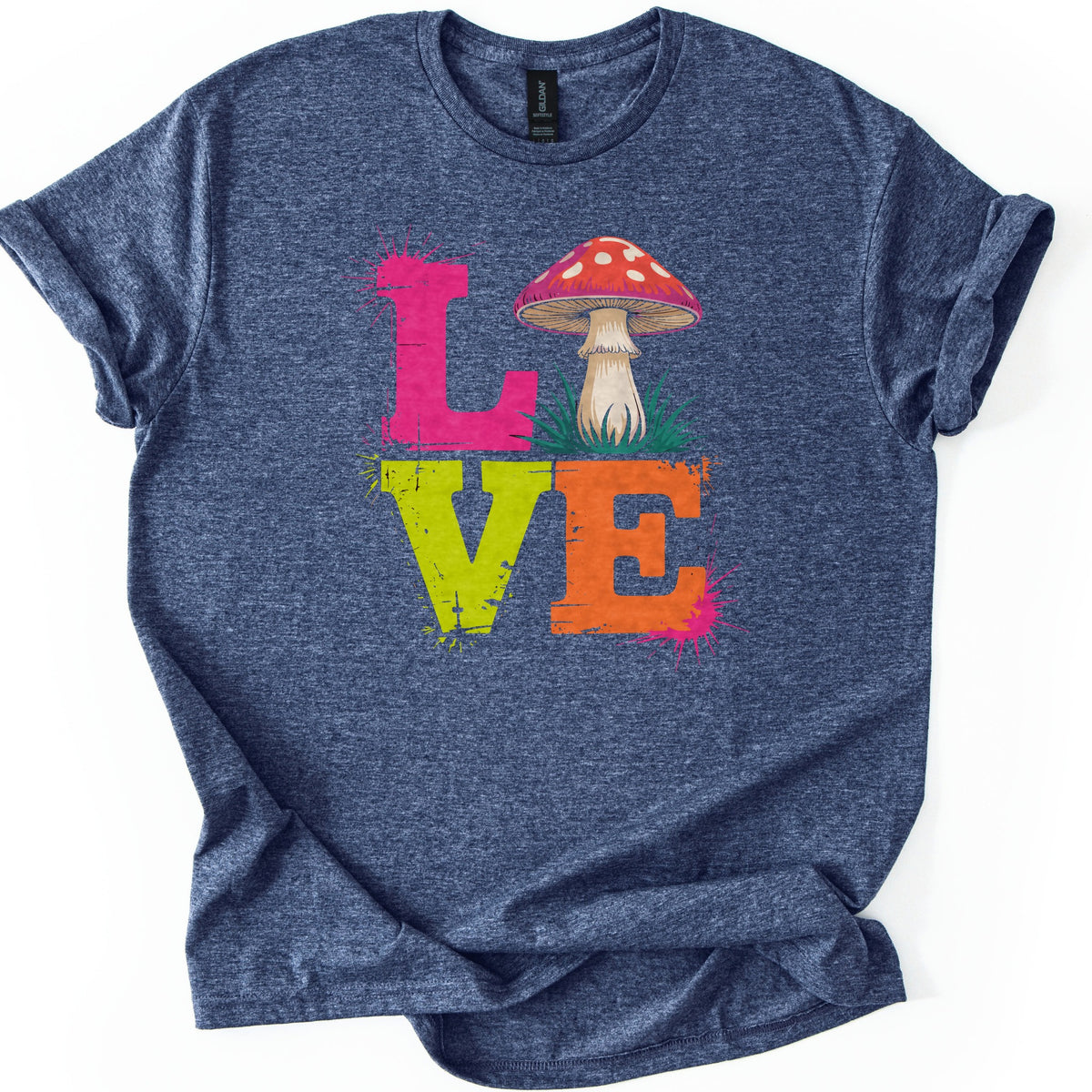 Mushroom Love Comfort Colors T-shirt in Heather Navy, laid flat. The word LOVE in stacked distressed letters: a pink L, a red mushroom with white spots in green grass for the O, a lime green V and an orange E, with paint splatters. The shirt lies on white with cuffed sleeves.