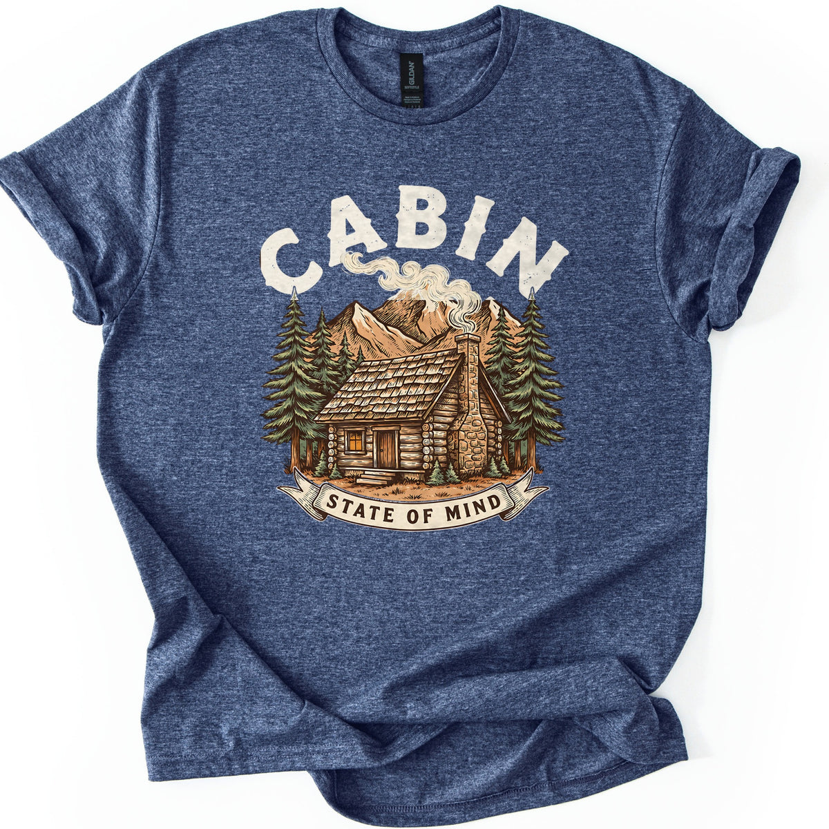 Cabin State Of Mind Comfort Colors T-shirt in Heather Navy, laid flat. CABIN arches in distressed cream letters over a log cabin with a smoking stone chimney, pine trees and mountains, above a banner reading STATE OF MIND. The shirt lies on white with cuffed sleeves.