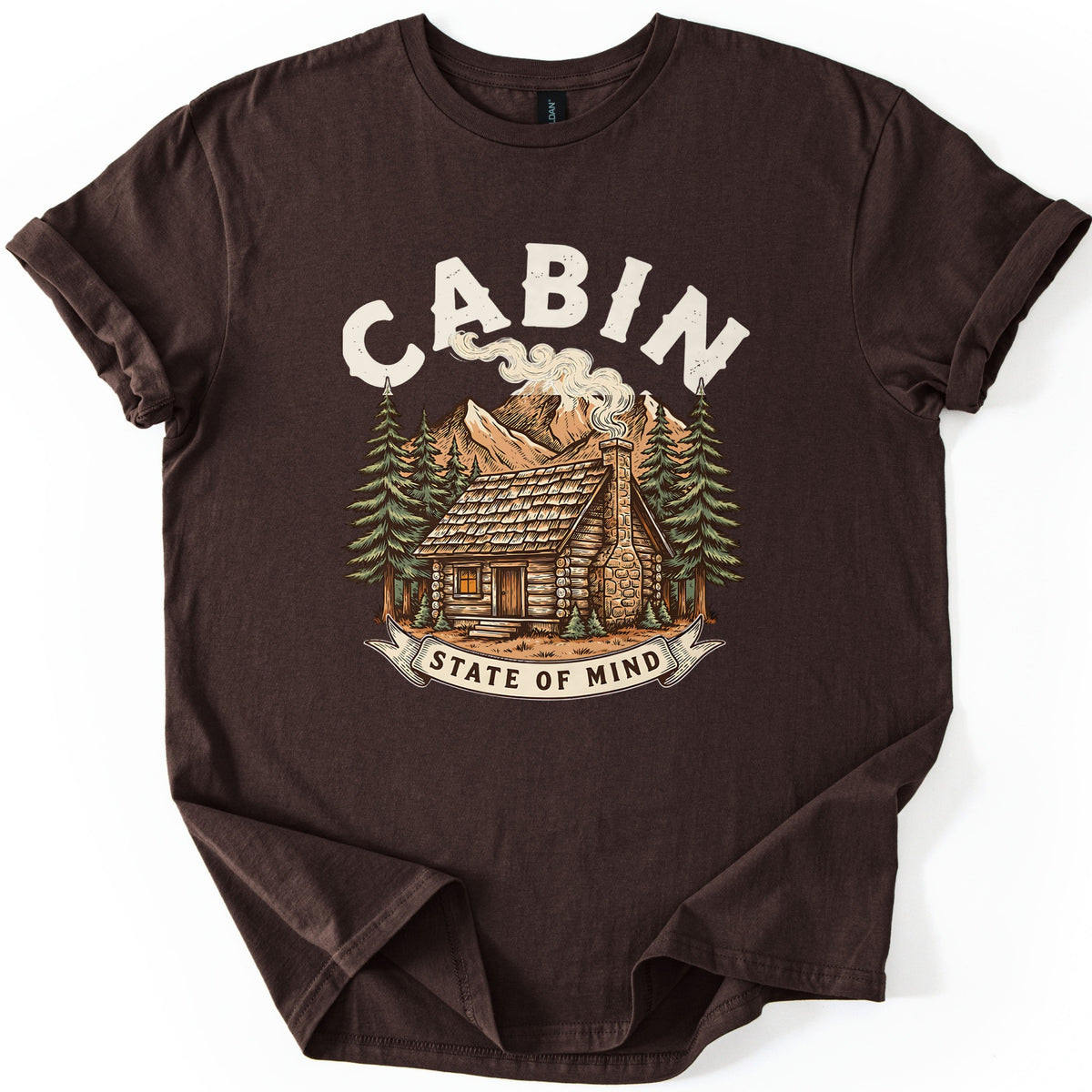 Cabin State Of Mind Comfort Colors T-shirt in Dark Chocolate, laid flat. CABIN arches in distressed cream letters over a log cabin with a smoking stone chimney, pine trees and mountains, above a banner reading STATE OF MIND. The shirt lies on white with cuffed sleeves.