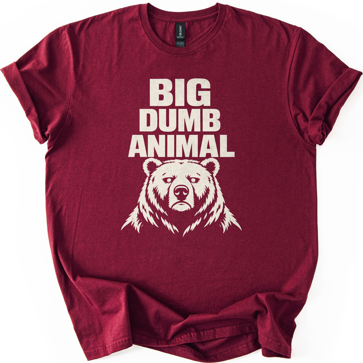 Big Dumb Animal Comfort Colors T-shirt in Maroon, laid flat. Bold cream letters read BIG DUMB ANIMAL above a cream illustration of a stern, front-facing bear head with shaggy fur. The sleeves are rolled and the shirt lies on a white background.