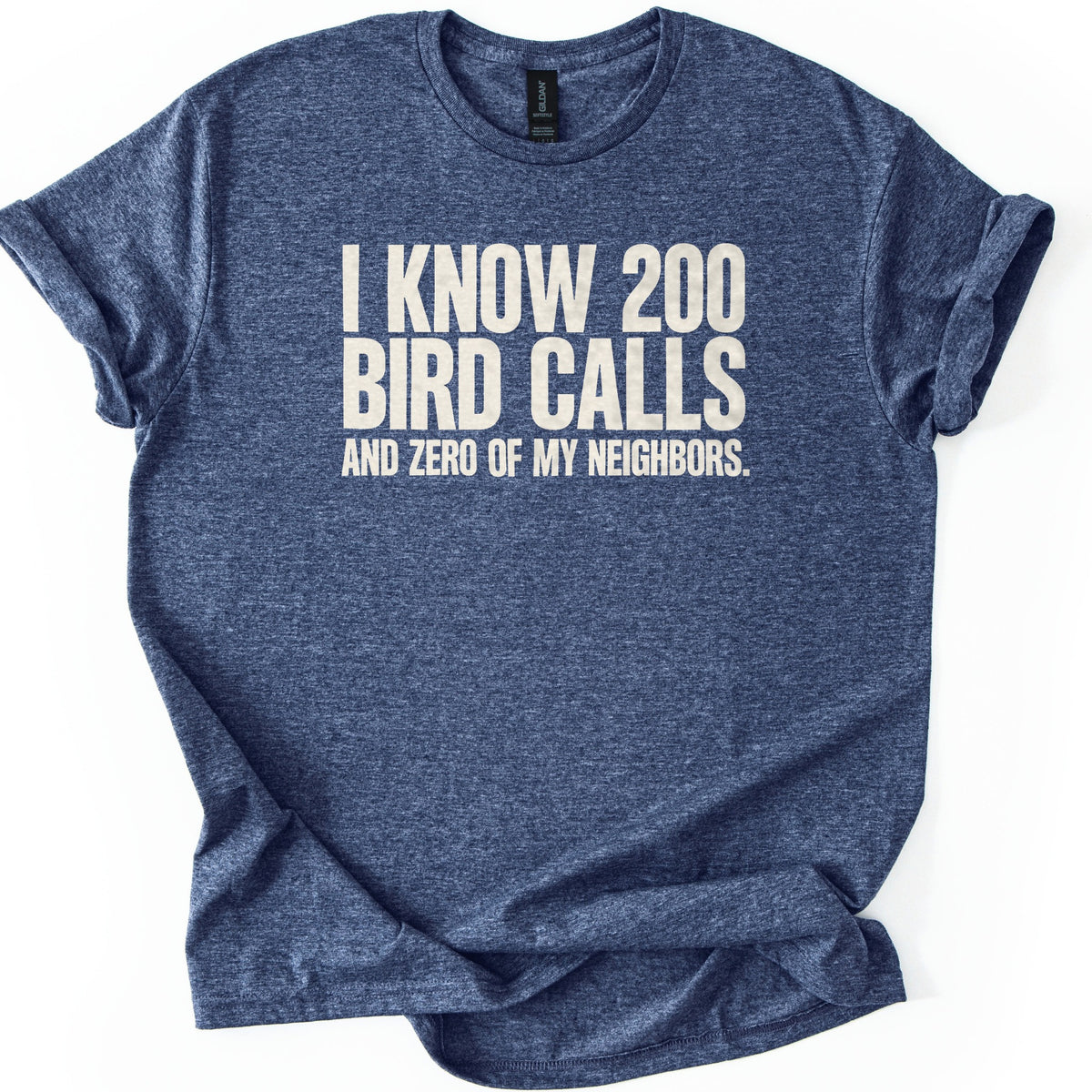 I Know 200 Bird Calls and Zero of My Neighbors Comfort Colors T-shirt in Heather Navy, laid flat. Bold cream capital letters across the chest read I Know 200 Bird Calls and Zero of My Neighbors. The heathered shirt lies on a white background with rolled sleeves and a rumpled hem.
