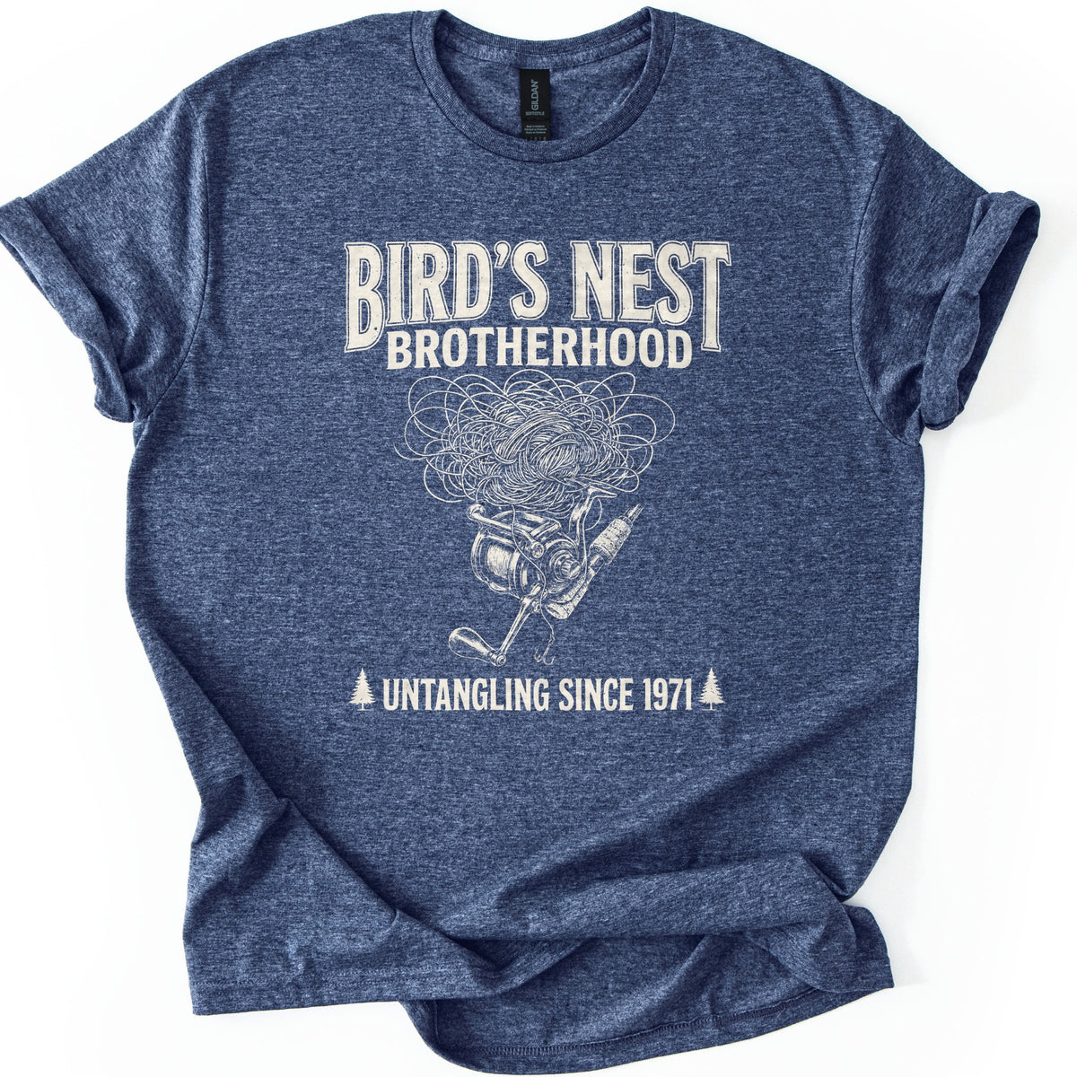 Birds Nest Brotherhood Comfort Colors T-shirt in Heather Navy, laid flat. Cream print reads Bird's Nest Brotherhood above a tangled mess of fishing line over a spinning reel, rod and hook, then Untangling Since 1971 between two pine trees. Sleeves cuffed, on a white backdrop.