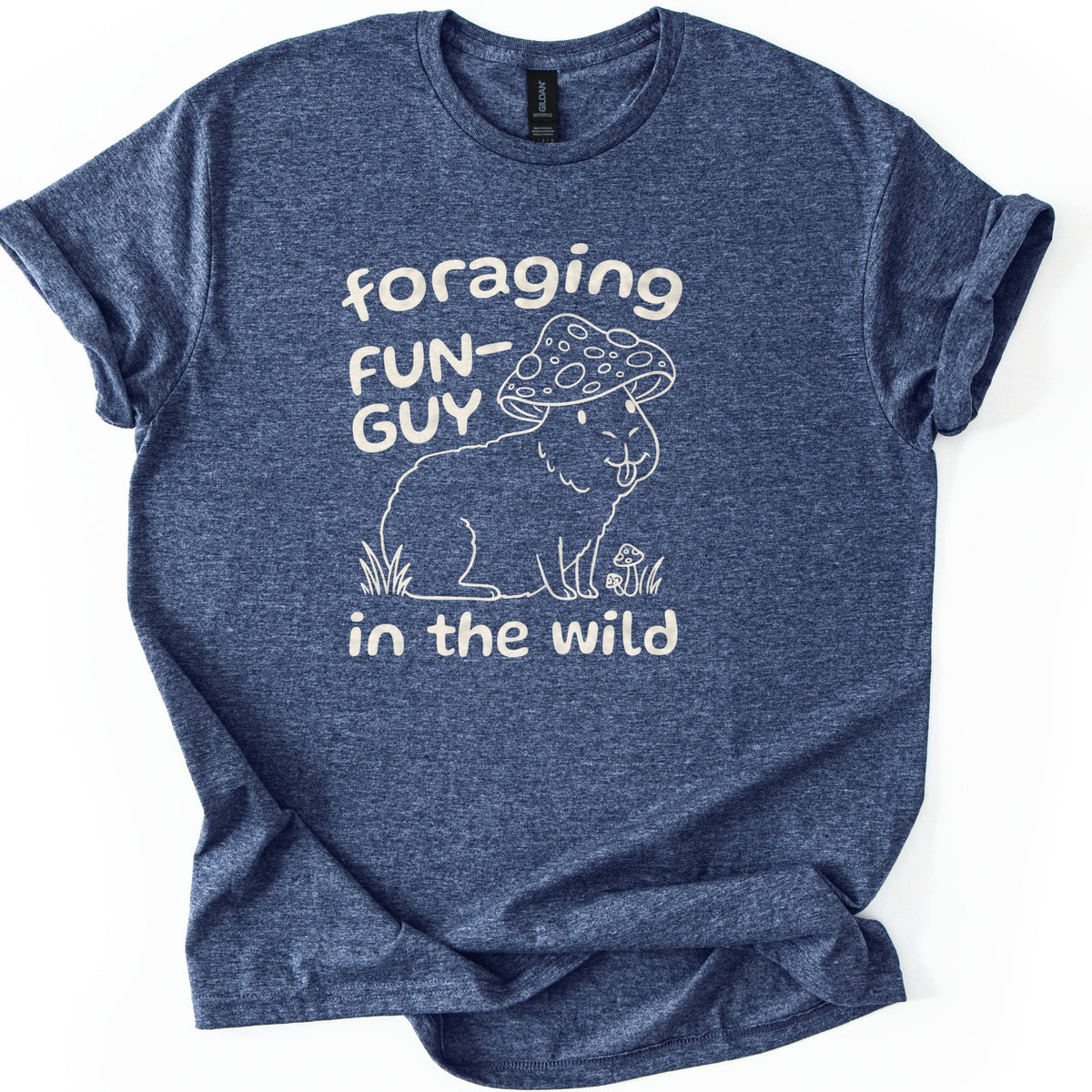 Foraging Fun-Guy Capybara Comfort Colors T-shirt in Heather Navy, laid flat. A cream line drawing of a winking capybara with its tongue out, wearing a spotted mushroom cap and sitting in grass by tiny mushrooms, with the words foraging FUN-GUY in the wild. Sleeves rolled, on white.