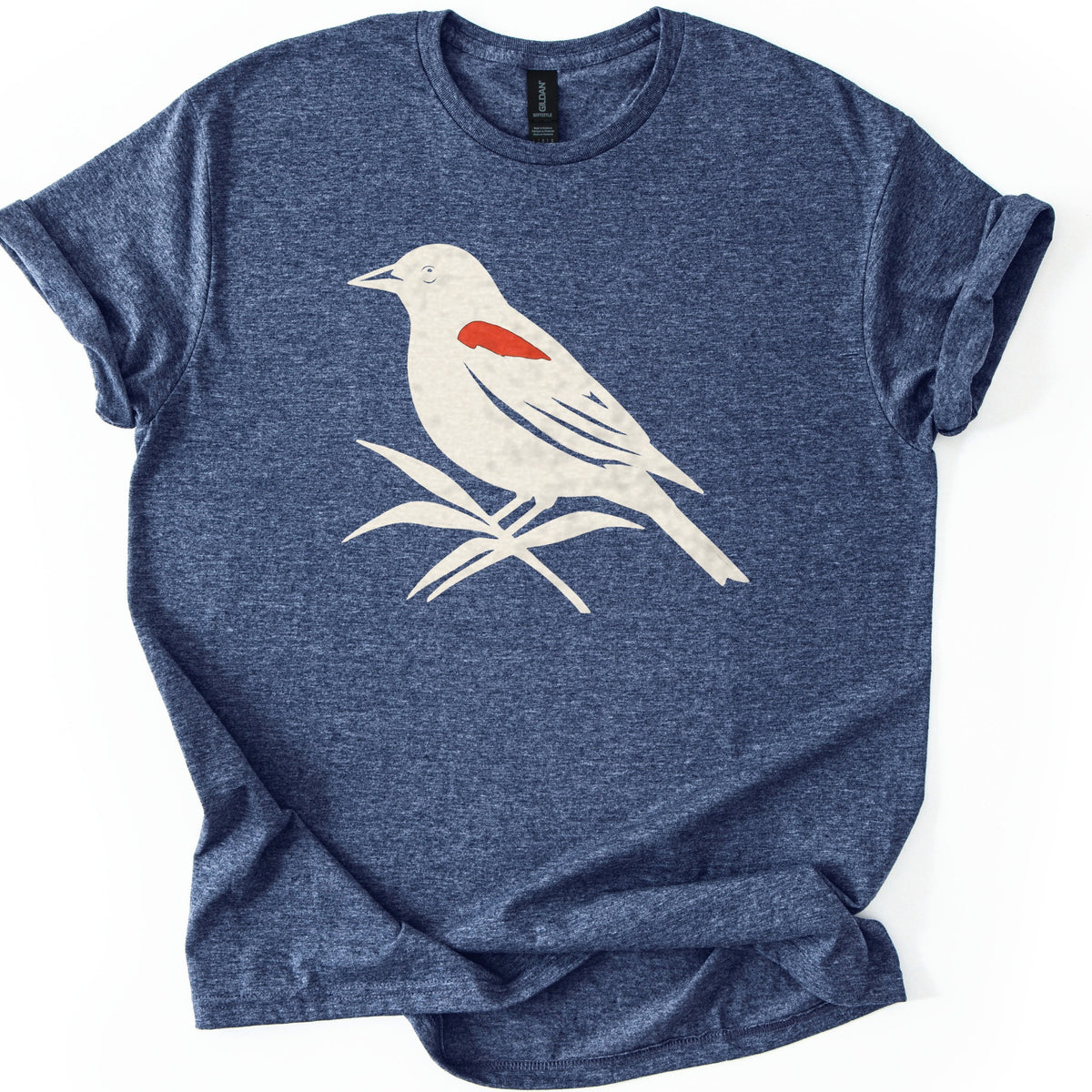 Red Winged Blackbird Comfort Colors T-shirt in Heather Navy, laid flat. A cream silhouette of a red-winged blackbird with a red shoulder patch, perched on slender leaves, with no words. The shirt has rolled sleeves and lies on a white background.