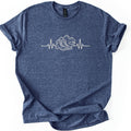 Hiking Heartbeat Comfort Colors T-shirt in Heather Navy, laid flat. A cream line drawing of a heartbeat line that turns into a pair of hiking boots in front of mountains, a winding trail and two pine trees; no words. Sleeves are cuffed on a white background.