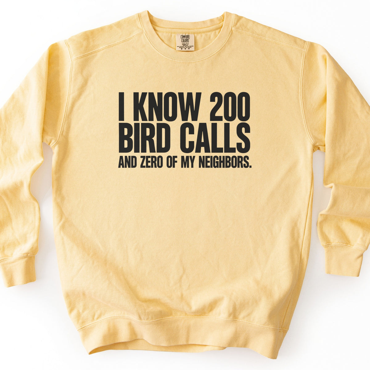 I Know 200 Bird Calls and Zero of My Neighbors Comfort Colors crewneck sweatshirt in Butter, laid flat. Bold black capital letters across the chest read I Know 200 Bird Calls, with And Zero of My Neighbors. in smaller letters below. The sweatshirt lies on a plain white background.
