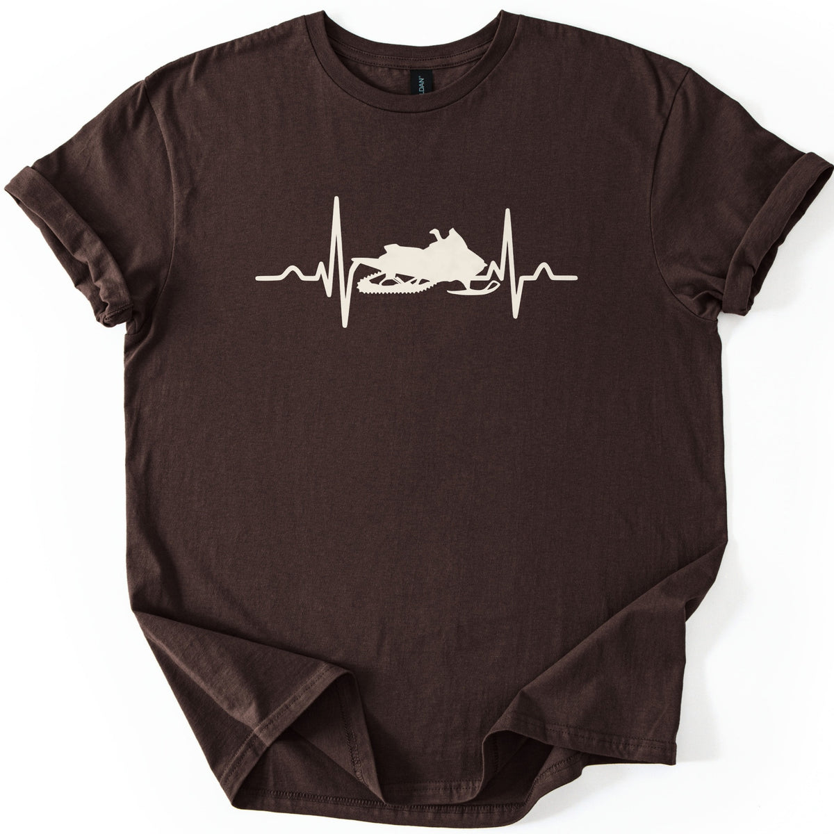 Heartbeat Snowmobile Comfort Colors T-shirt in Dark Chocolate, laid flat. A cream heartbeat line crosses the chest, with a snowmobile silhouette in the center of the pulse and no words. The shirt has cuffed sleeves and lies on a white background.