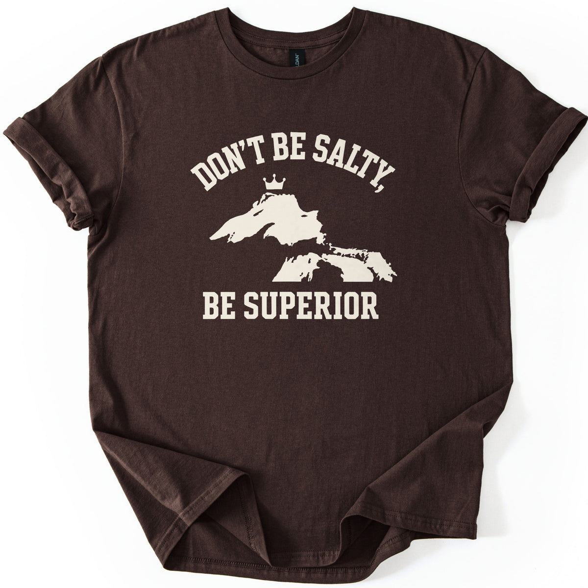 Be Superior Comfort Colors T-shirt in Dark Chocolate, laid flat. A cream print shows the words Don't Be Salty, arched over a silhouette of the Great Lakes with a small crown above Lake Superior, and Be Superior below. Sleeves are cuffed on a white background.