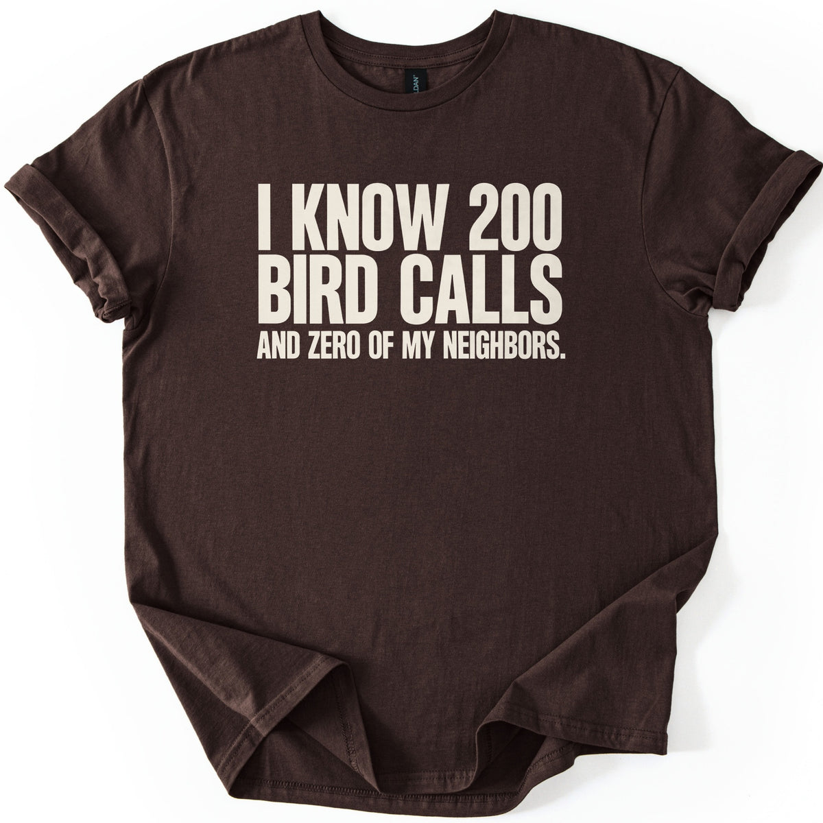 I Know 200 Bird Calls and Zero of My Neighbors Comfort Colors T-shirt in Dark Chocolate, laid flat. Bold cream capital letters across the chest read I Know 200 Bird Calls and Zero of My Neighbors. The shirt lies on a white background with rolled sleeves and a loosely rumpled hem.