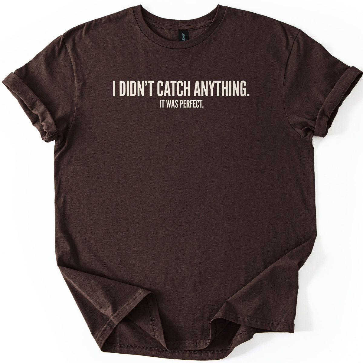 Didn't Catch Anything Comfort Colors T-shirt in Dark Chocolate, laid flat. Cream block letters across the chest read I DIDN'T CATCH ANYTHING. with smaller text below reading IT WAS PERFECT. The shirt has cuffed sleeves and lies on a white background.