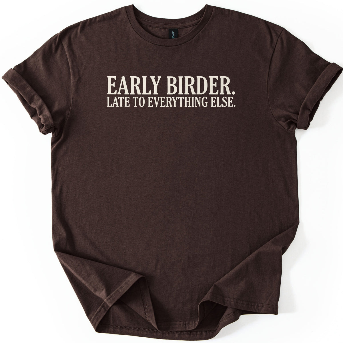 Early Birder Comfort Colors T-shirt in Dark Chocolate, laid flat. Cream serif capital letters across the chest read EARLY BIRDER. LATE TO EVERYTHING ELSE. The shirt lies on a white background with its short sleeves rolled up.