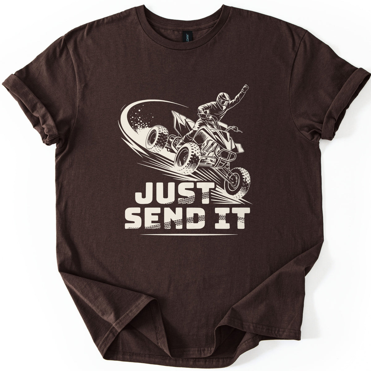 ATV Just Send It Comfort Colors T-shirt in Dark Chocolate, laid flat. A cream drawing of a helmeted rider jumping a quad ATV with a raised fist and a dust trail, above the words Just Send It in tire-tread lettering. Sleeves are cuffed, on a white background.