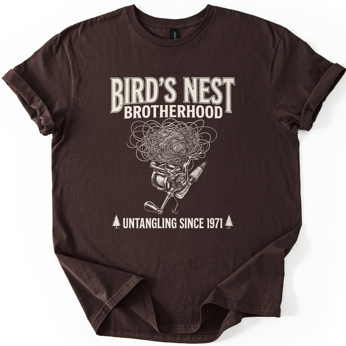 Birds Nest Brotherhood Comfort Colors T-shirt in Dark Chocolate, laid flat. Cream print reads Bird's Nest Brotherhood above a tangled mess of fishing line over a spinning reel, rod and hook, then Untangling Since 1971 between two pine trees. Sleeves cuffed, on a white backdrop.
