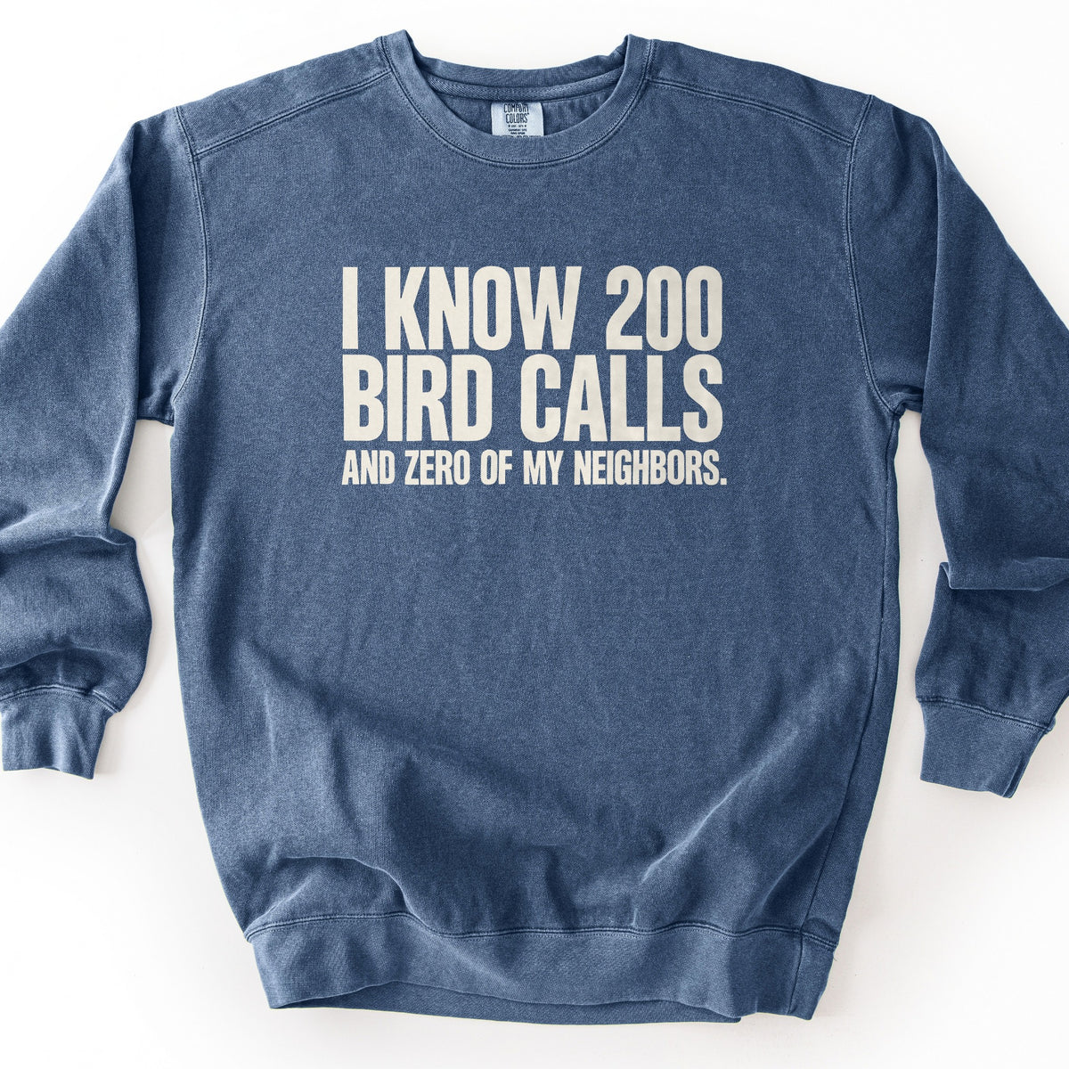 I Know 200 Bird Calls and Zero of My Neighbors Comfort Colors crewneck sweatshirt in Denim, laid flat. Off-white block lettering on the chest reads I Know 200 Bird Calls in large letters, with And Zero of My Neighbors. in smaller letters below. The sweatshirt lies flat on a plain white background.