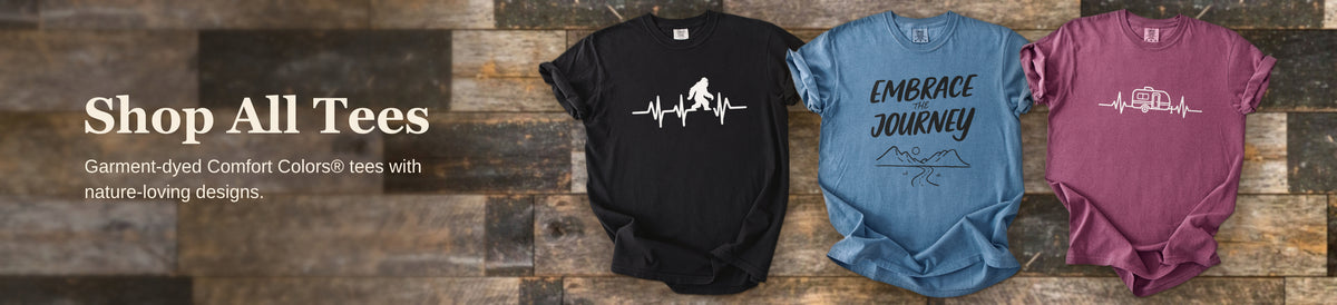 Three Comfort Colors graphic tees arranged against rustic barnwood