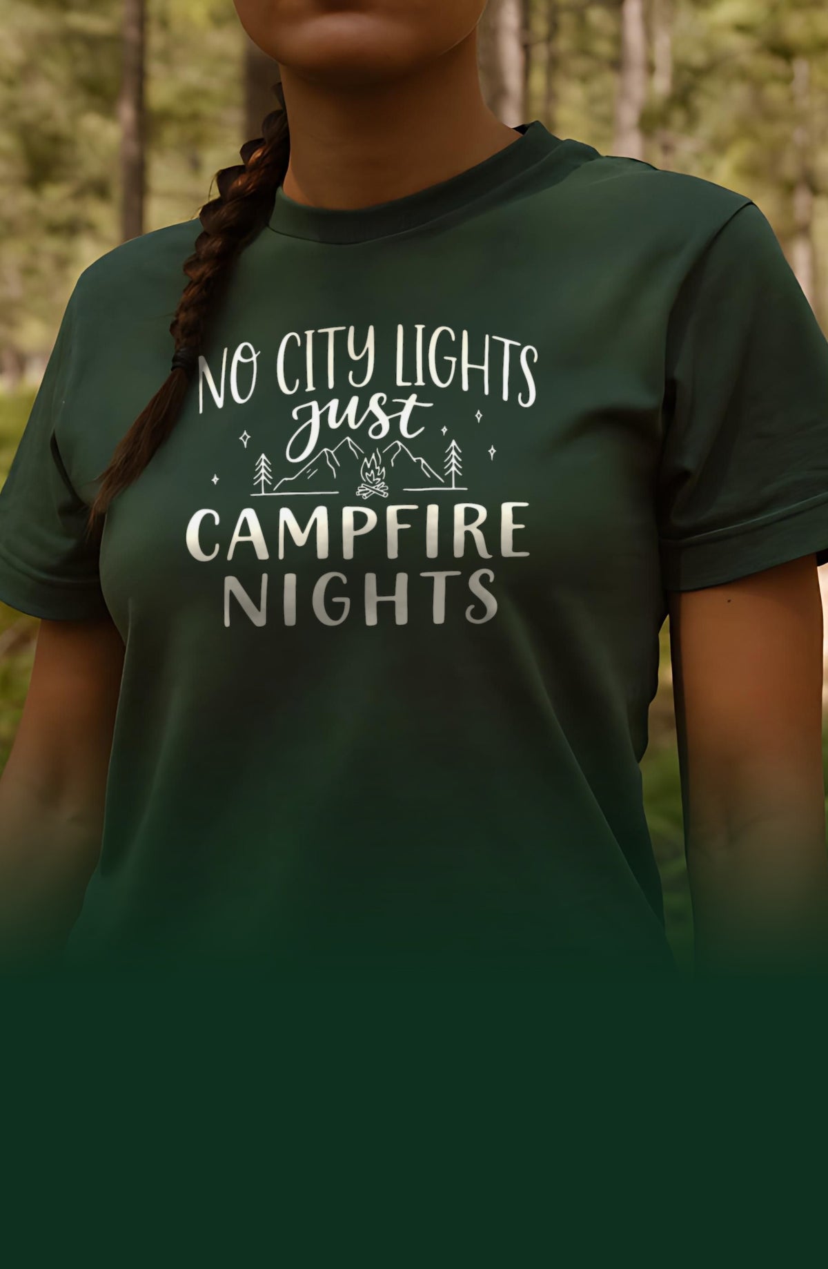 Woman in a forest green t-shirt printed with the Campfire Nights design, standing on a sunlit forest trail